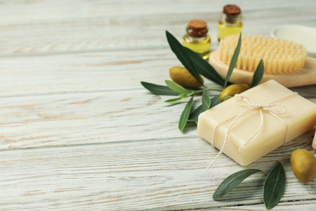 Natural soap bar with olives, brush, oil and green leaves on white wooden table, closeup. Space for textの写真素材