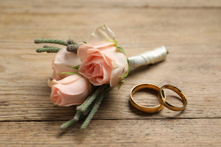 Gold wedding rings and stylish boutonniere on wooden table, closeup