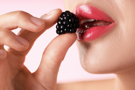 Woman with lipstick on her lips and blackberry against pink background, macro view