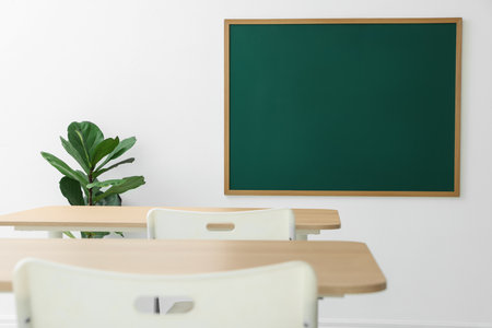 Blank green chalkboard, desks, chairs and plant in classroomの写真素材