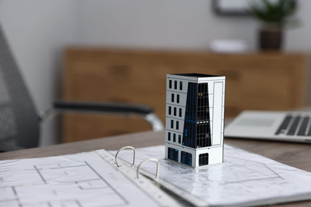 Real estate. Apartment building model, architectural drawings and laptop on table indoors, closeup....