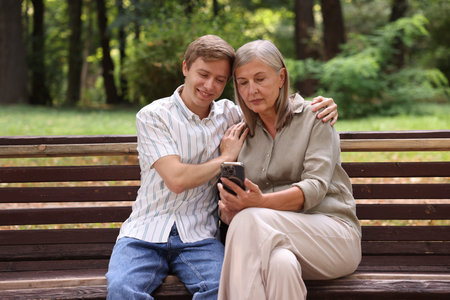 Mother and her son using smartphone on bench in parkの写真素材