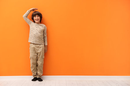 Cute boy measuring his height near orange wall indoors. Space for textの写真素材