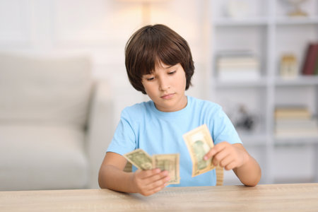 Boy with pocket money at wooden table indoorsの写真素材