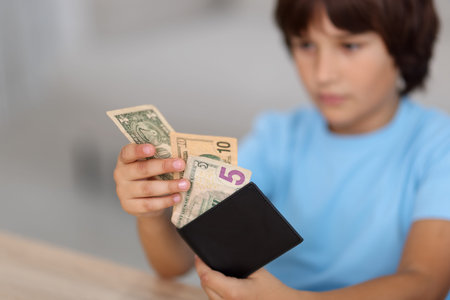 Boy with pocket money at wooden table indoors, selective focus