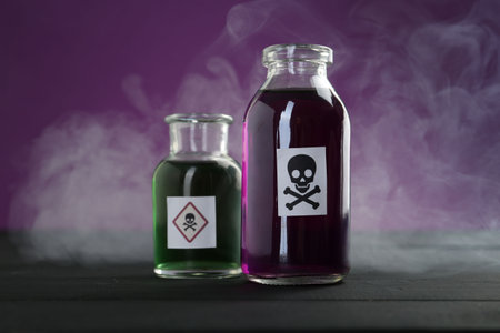 Bottles with warning signs and smoke on black wooden table against purple background, closeupの写真素材
