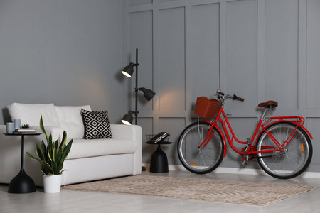 Red bicycle, lamp and cozy sofa near gray wall indoorsの写真素材