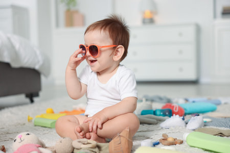 Cute baby with sunglasses and different accessories on floor at homeの写真素材