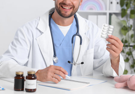 Pediatrician with pills and clipboard at desk in clinic, closeupの写真素材