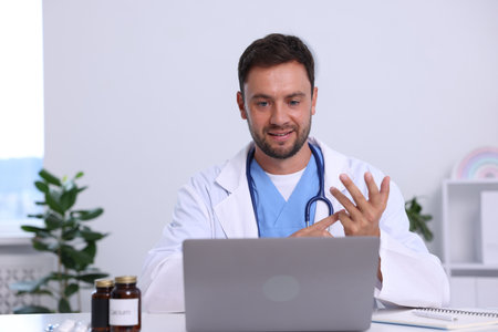 Pediatrician having video call with patient via laptop at desk in hospitalの写真素材