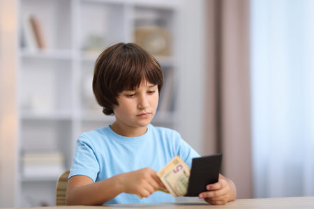 Boy with pocket money at wooden table indoors. Space for text