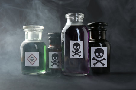 Bottles of poison with warning signs and smoke on dark background, closeupの写真素材