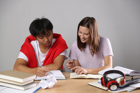 Students with books preparing for exam at table near gray wallの写真素材