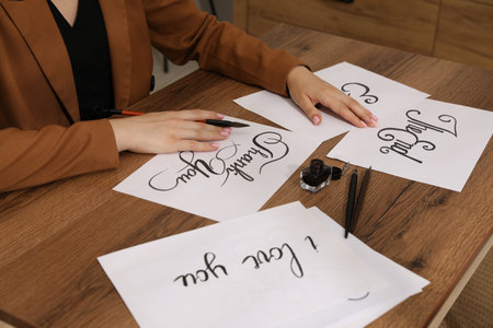 Woman with calligraphy tools and handwritten cards at wooden table indoors, closeupの写真素材