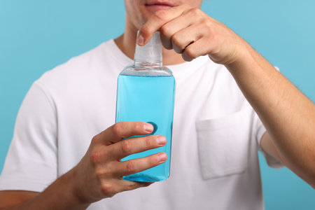 Man with bottle of mouthwash on blue background, closeupの写真素材