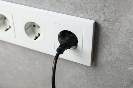 Power plug in socket on gray wall, closeup