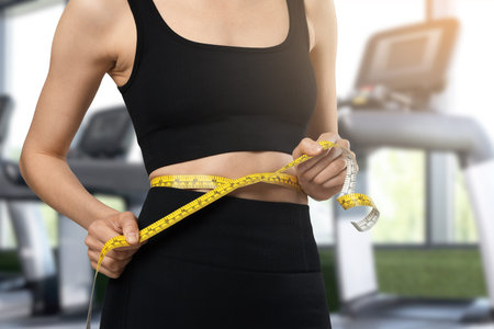 Athletic woman with flat belly and measuring tape in gym, closeup