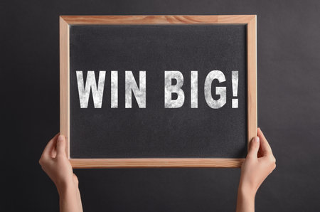 Woman holding chalkboard with phrase Win Big against dark background, closeupの写真素材