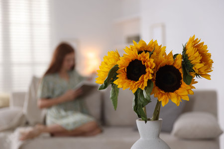 Girl reading book at home, focus on beautiful sunflowers in vaseの写真素材