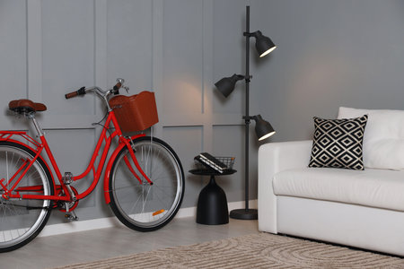 Red bicycle, lamp and cozy sofa near gray wall indoorsの写真素材