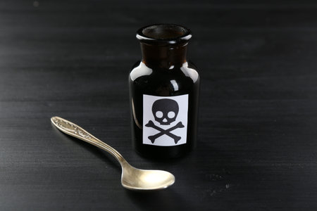 Bottle of poison with warning sign and spoon on black wooden table, closeupの写真素材