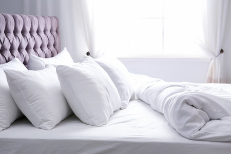 Modern bed with soft pillows near windowの写真素材