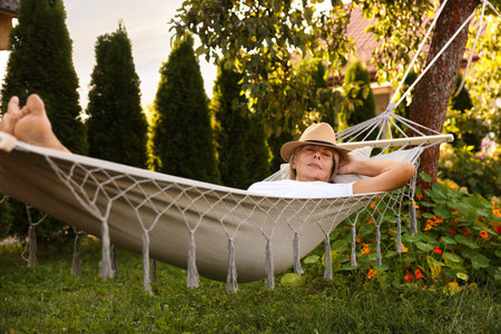 Senior woman in straw hat resting in hammock outdoorsの写真素材