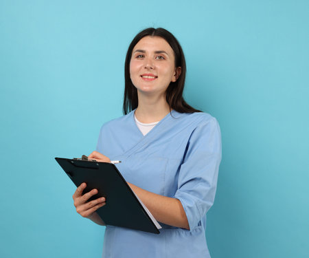 Nurse with clipboard taking notes on light blue backgroundの写真素材
