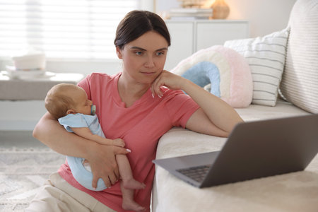 Telehealth. Mother with her baby leaning on sofa and having online consultation with doctor at homeの写真素材
