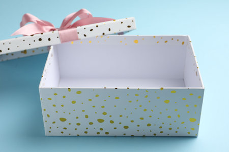 Opened gift box with beautiful lid on light blue background, closeup