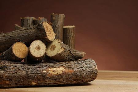 Pile of cut firewood on wooden table against brown background, closeup. Space for text