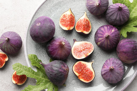 Fresh ripe figs and green leaves on gray textured table, flat lay