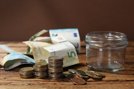 Glass jar with coins and banknotes on wooden table, closeup