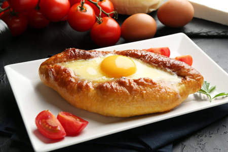Tasty khachapuri with cheese, eggs and tomatoes on black table, closeup