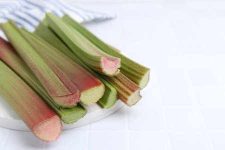Fresh rhubarb stalks on white tiled table, closeup. Space for text