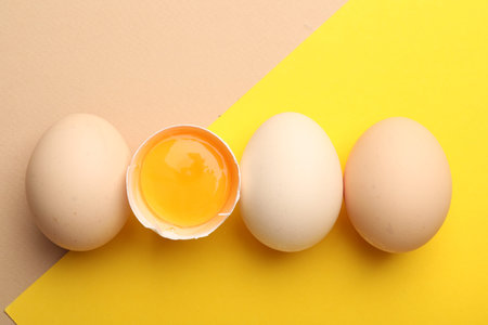 Whole and broken chicken eggs on color background, flat lay