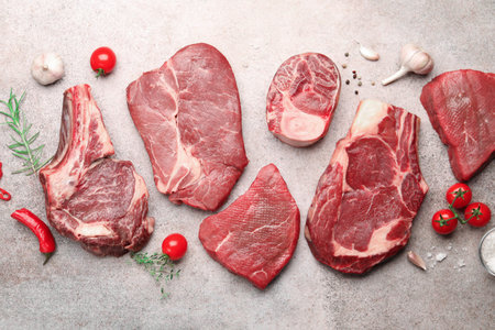 Pieces of raw beef meat, spices and tomatoes on gray table, flat lay