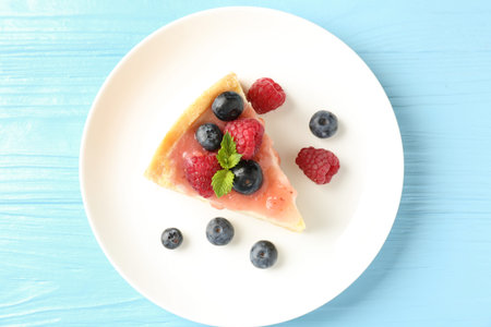 Piece of tasty cheesecake with berries and sauce on light blue wooden table, top viewの写真素材