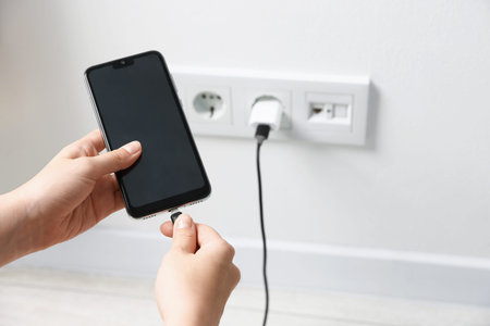 Woman connecting charging cable to smartphone indoors, closeup