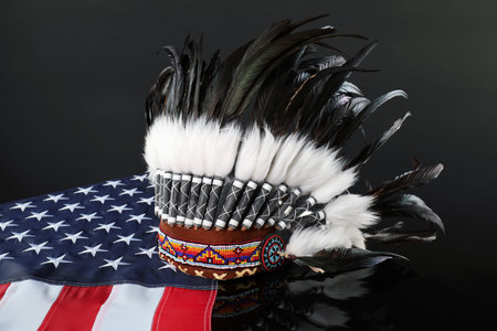 Traditional warbonnet (Native American chief headdress) and flag of USA on black mirror surface