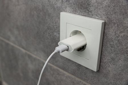 USB adapter with cable plugged into electric socket on gray wall, closeup. Space for text