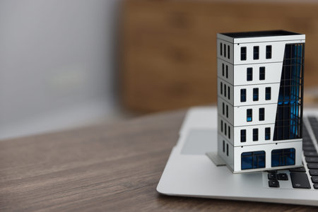 Real estate. Apartment building model and laptop on table indoors, closeup. Space for text
