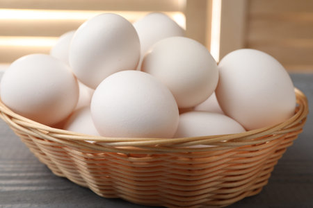 Raw chicken eggs in wicker basket on gray wooden table indoors, closeup