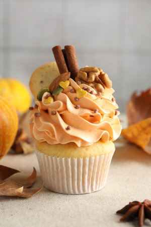 Delicious cupcake with color cream, spices, cookie, nuts and autumn decor on grey table, closeupの写真素材
