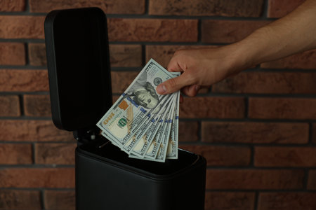 Man throwing dollar banknotes into trash bin near brick wall, closeupの写真素材