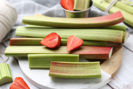 Rhubarb stalks and strawberries on white wooden table, closeup