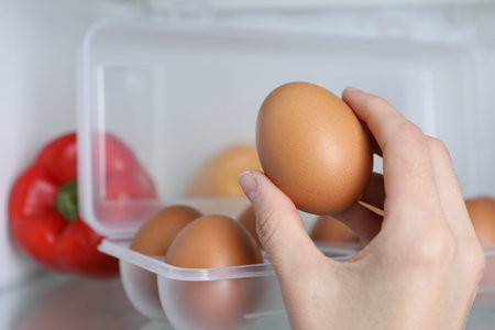 Woman taking raw chicken egg from refrigerator, closeup