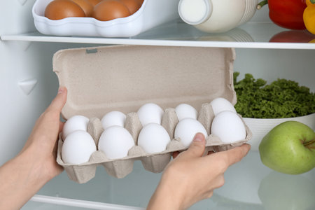 Woman taking egg carton with raw chicken eggs from refrigerator, closeup