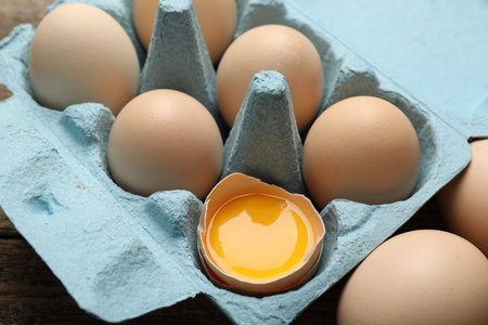 Whole and broken chicken eggs in egg carton on table, closeup
