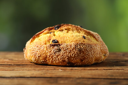 Loaf of fresh bread with sesame seeds and raisins on wooden table against blurred background,...